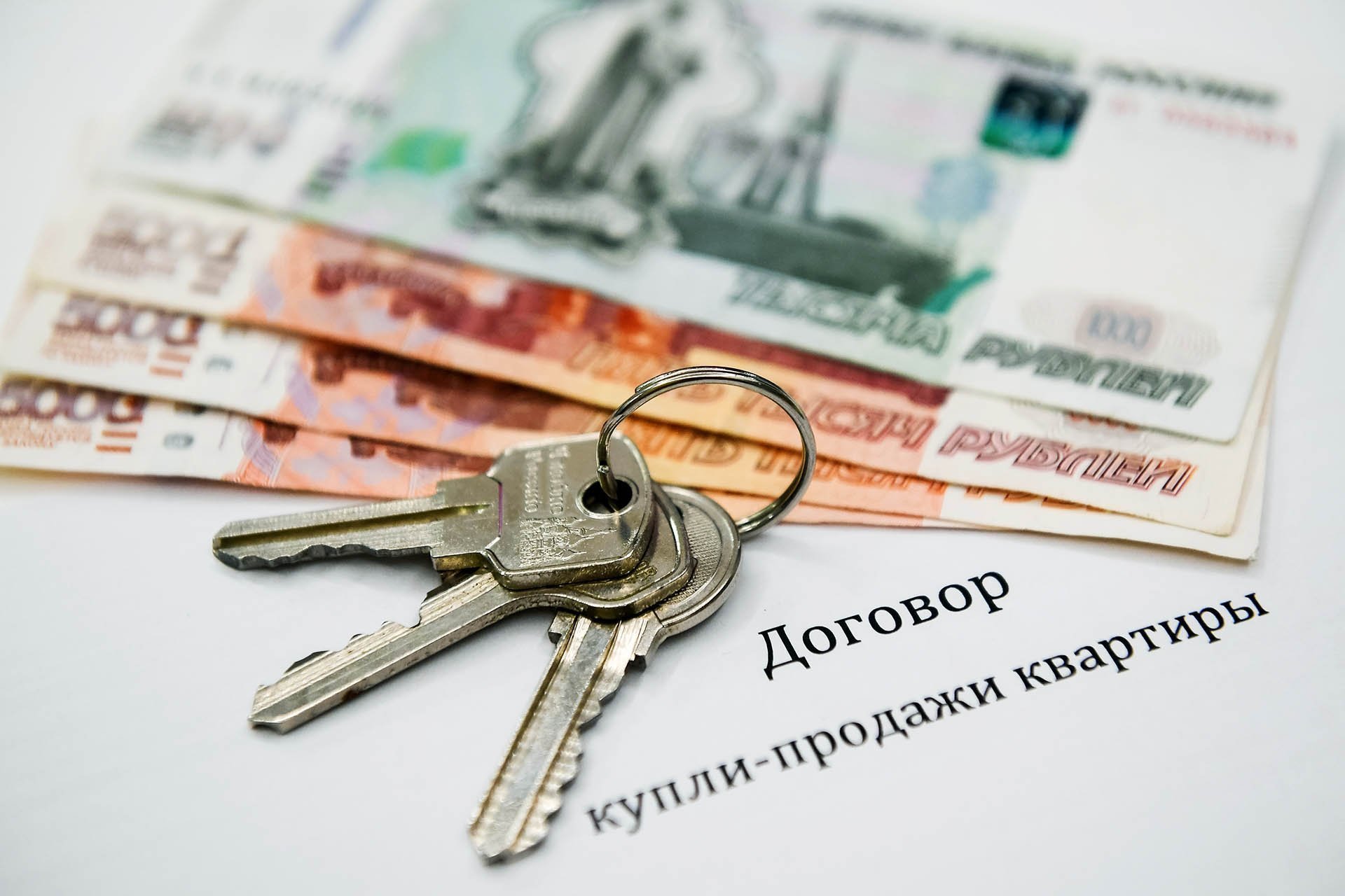 На договоре купли-продажи квартиры лежат денежные купюры и ключи