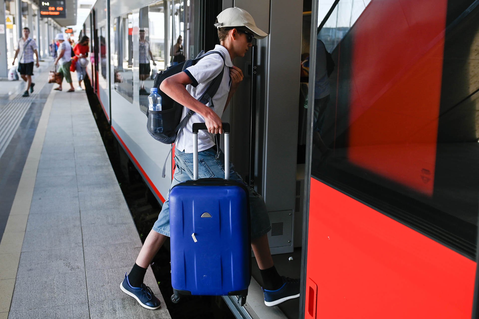 Пассажир-ребенок с чемоданом на железнодорожном вокзале заходит в поезд