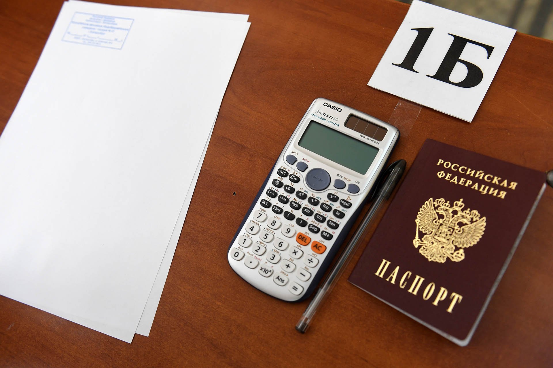 Паспорт, ручка, калькулятор и проштампованные листы для черновика на парте школьника