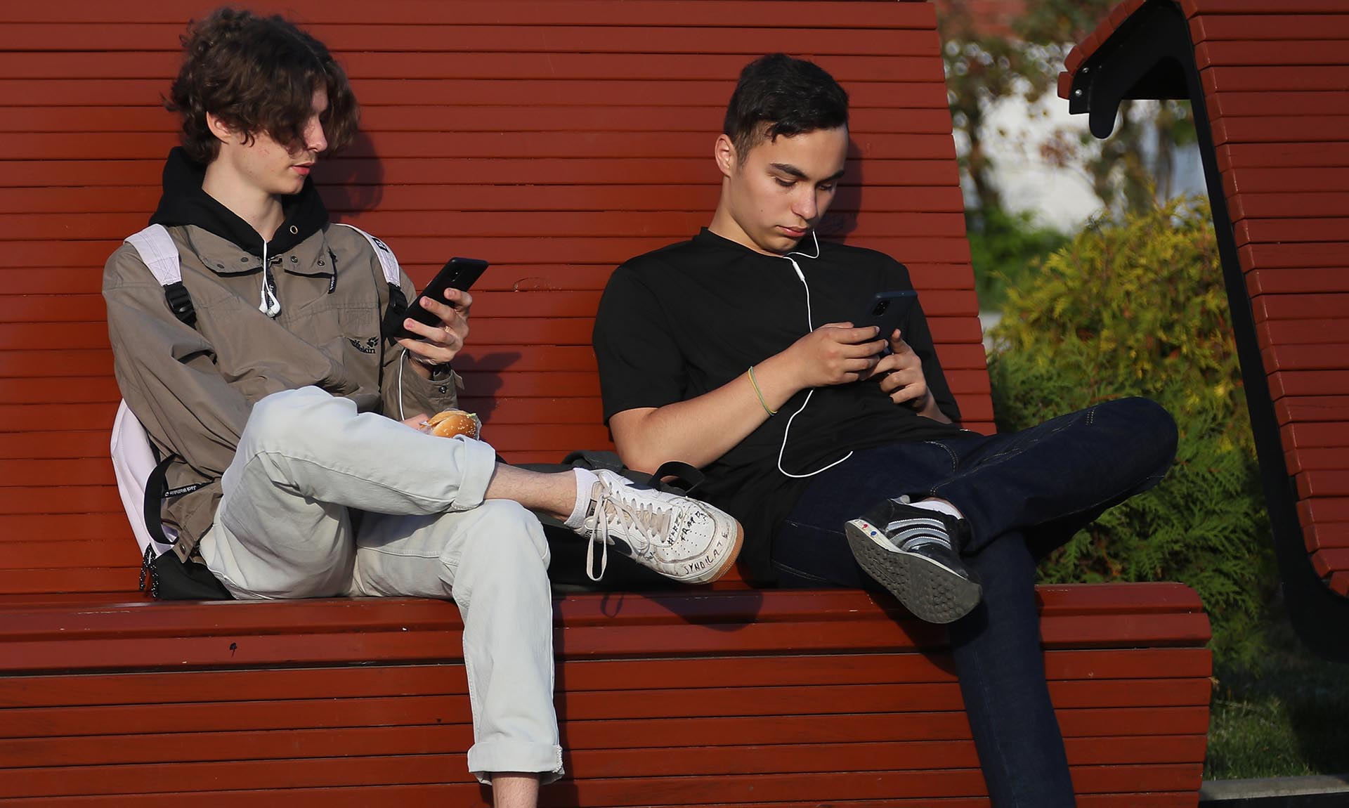 Подростки сидят на лавке с мобильными телефонами