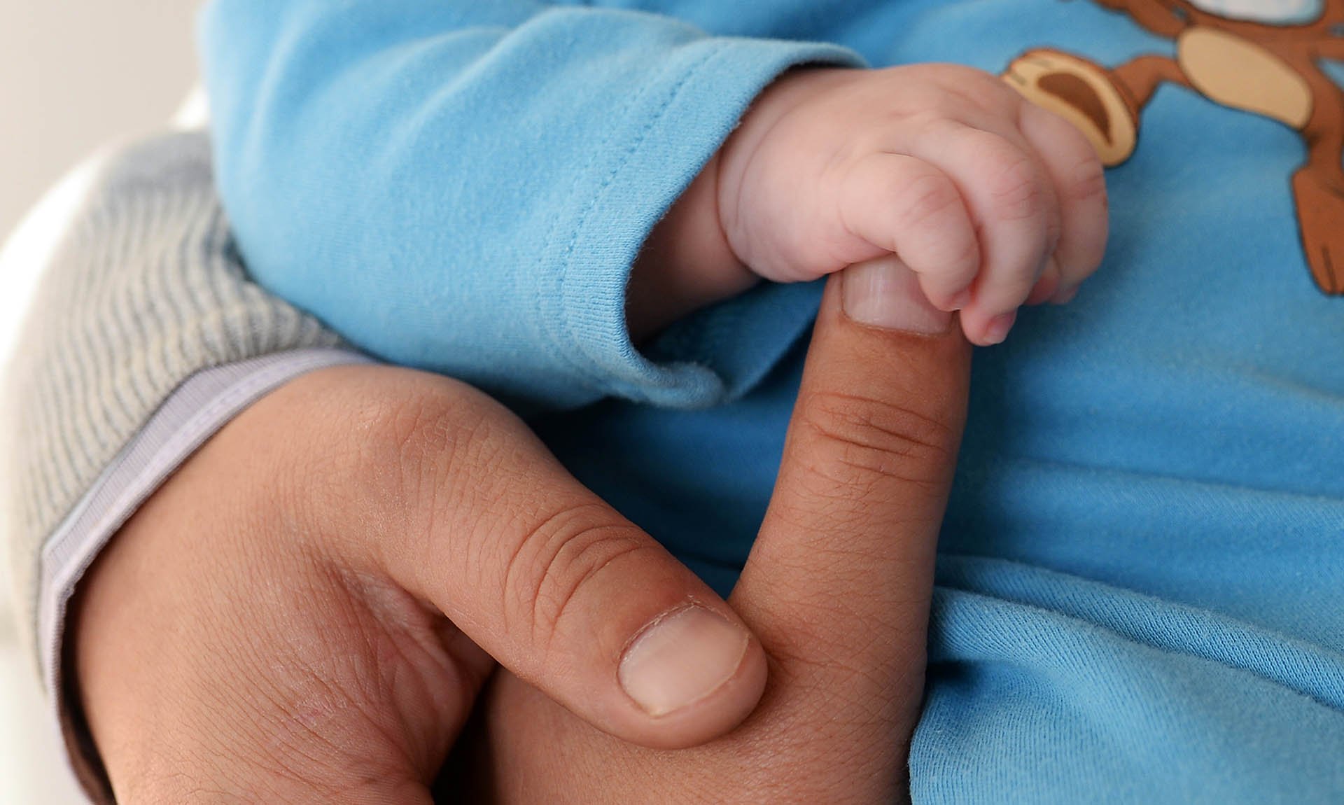 Крупный план младенец на руках держится за палец взрослого