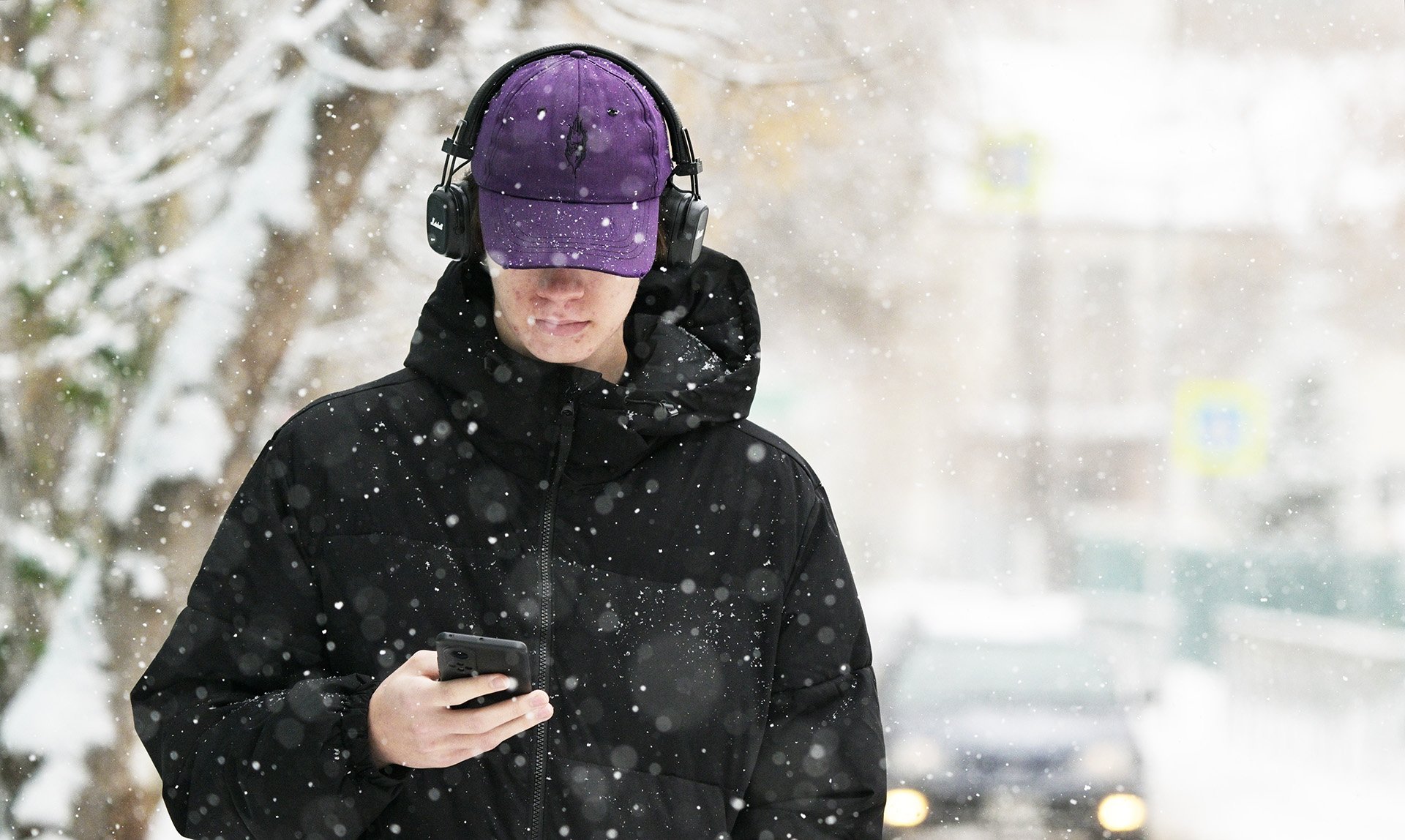Молодой человек с телефоном в наушниках в снежную погоду
