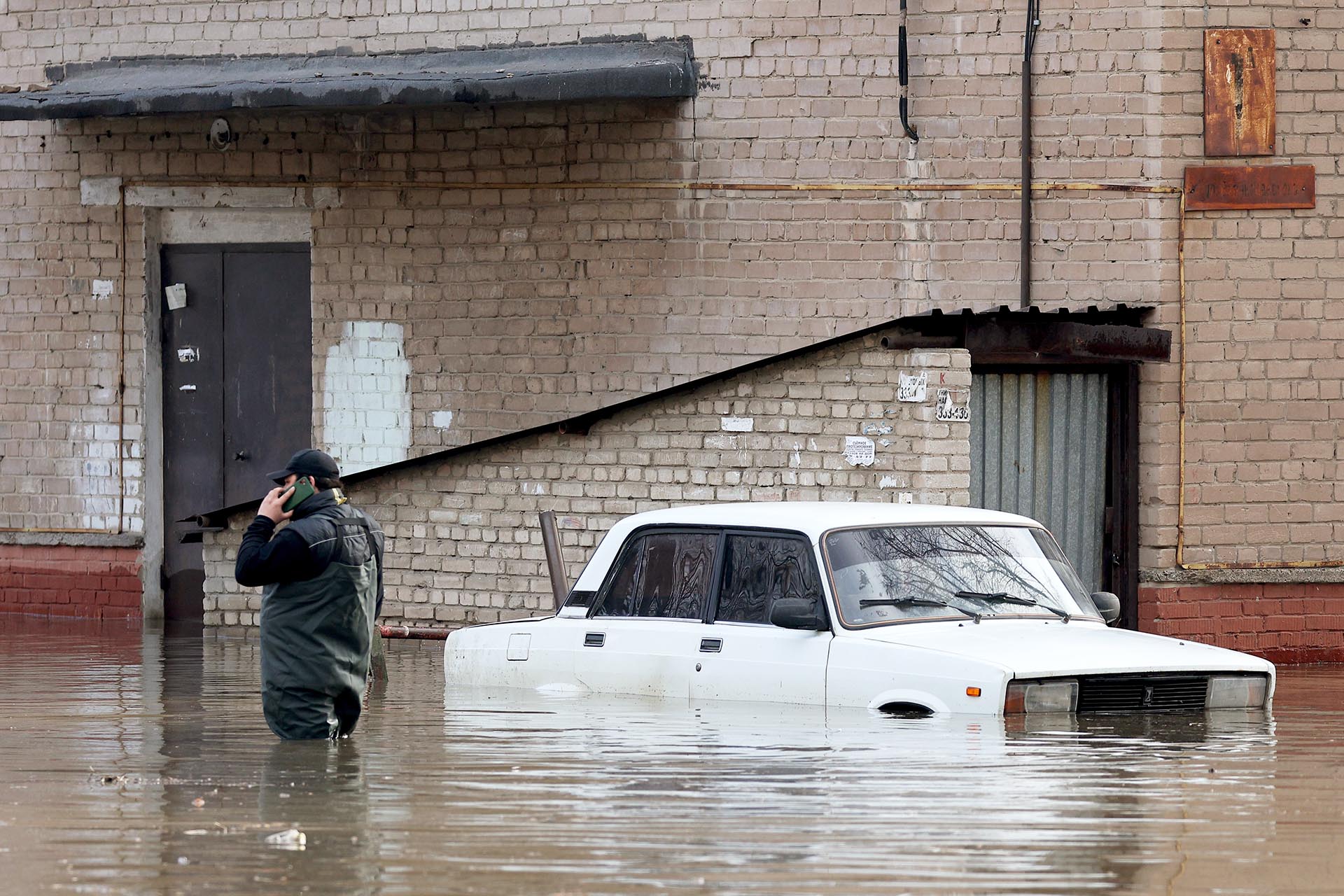 Мужчина стоит рядом с машиной на подтопленной улице