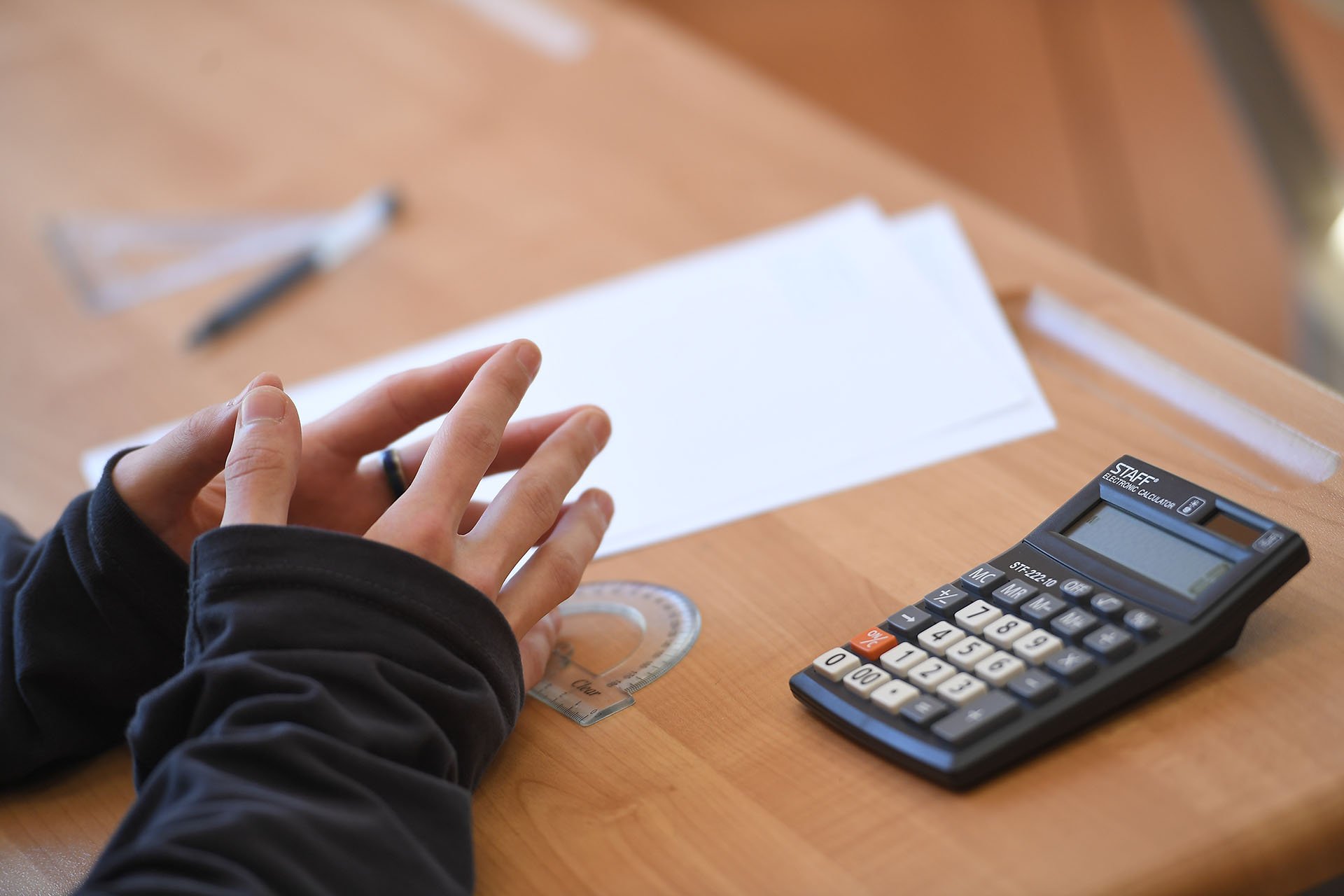 Крупный план руки, лист бумаги и калькулятор на школьной парте