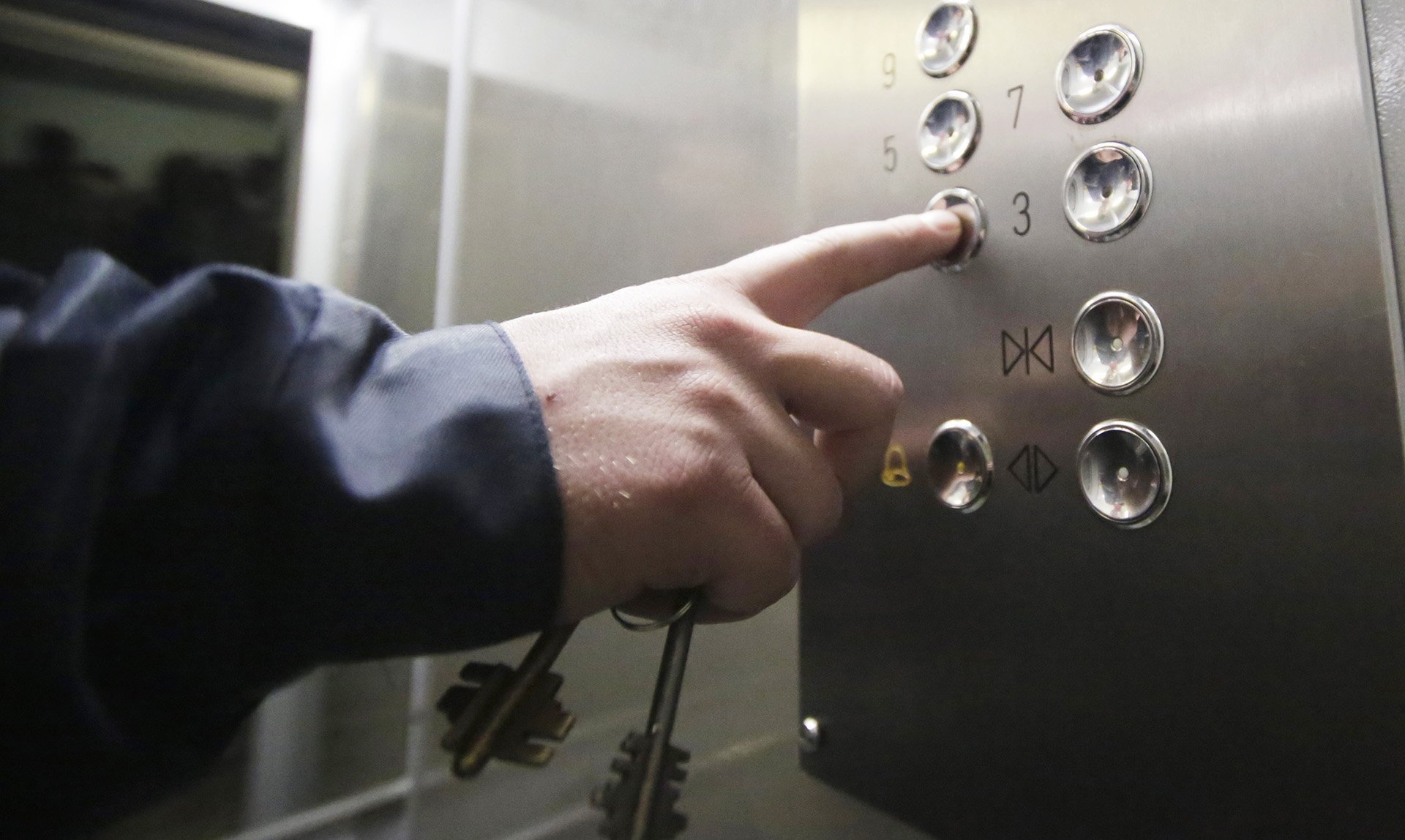 Мужчина нажимает кнопку этажа в лифте