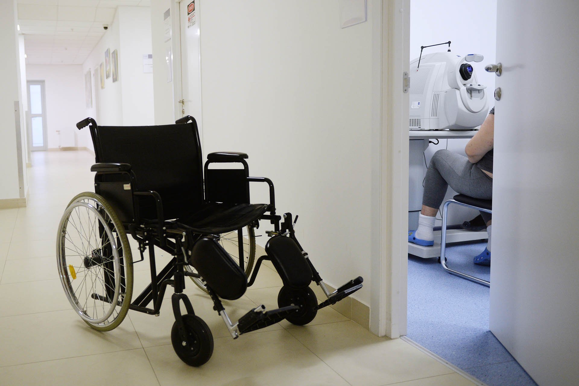 Инвалидная коляска в коридоре больницы у приоткрытой двери где проходит диагностика