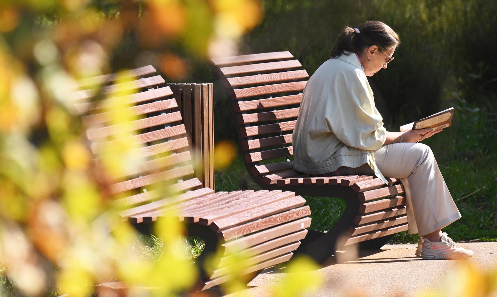 Пожилая женщина читает книгу на скамейке